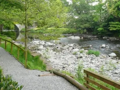 a wooden bench next to a river with a bridge at Keswick Bridge 22, within walking distance of Keswick town centre, strictly no pets in Keswick