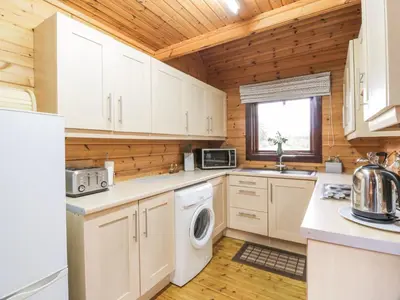 a kitchen with white cabinets and a washer and dryer at Moyle Lodge in Dalbeattie
