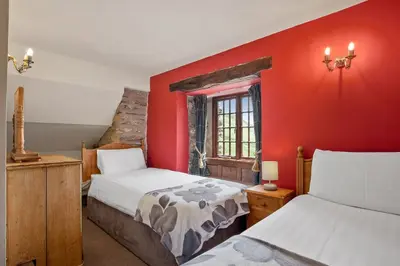 a bedroom with two beds and a red wall at The Mountain Cottages - Sawyers in Coniston