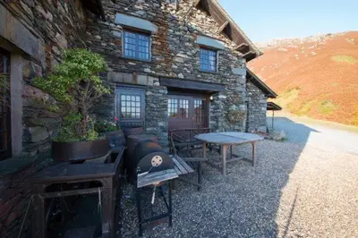 a stone building with a grill and a table in front of it at The Mountain Cottages - Sawyers in Coniston