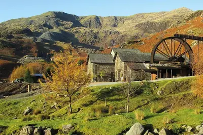 a building on a hill with mountains in the background at The Mountain Cottages - Pelton Wheel in Coniston