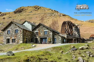a stone house on top of a hill with a building at The Mountain Cottages - Pelton Wheel in Coniston