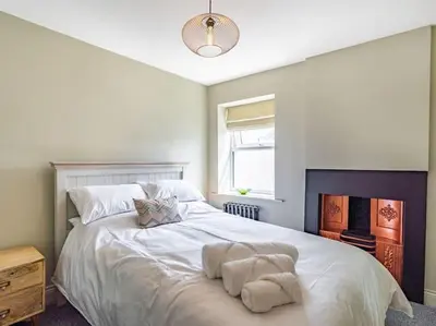 a bedroom with a large white bed with a fireplace at Northdene - 5 star Lake District Cottage in Cockermouth