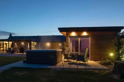 a small house with a patio at night at Amazing Cottage & detached Annex sleeps 8, Extra Deep Hot tub, Super Fast wifi, New for 2024 is the addition of Wood Fired Sauna in Castle Douglas