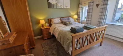 a bedroom with a bed and a dresser and two windows at Mains Street Retreat in Lockerbie