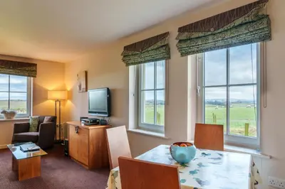 a living room with a table and chairs and windows at 12 Ullswater Suite - Whitbarrow Village in Penruddock