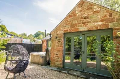 a brick house with a green door and a chair at Beckside Cottage, near Carlisle romantic cottage with hot tub in Longtown
