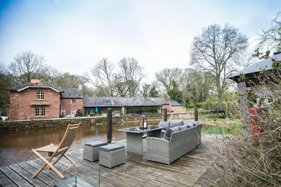 a wooden deck with a couch and chairs on the water at The Chard, Netherby, a micro cabin in a rural setting with a hot tub in Longtown