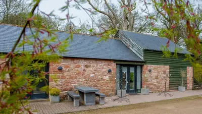 a brick building with a picnic table in front of it at The Heronry, Netherby, a luxurious cottage ideal for a romantic break with hot tub in a rural setting in Longtown