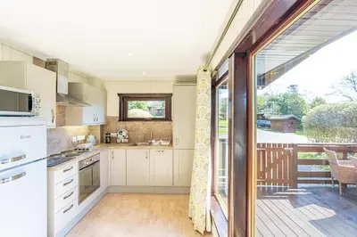a kitchen with white cabinets and a sliding glass door at Birch Lodge 12 with Hot Tub in Newton Stewart