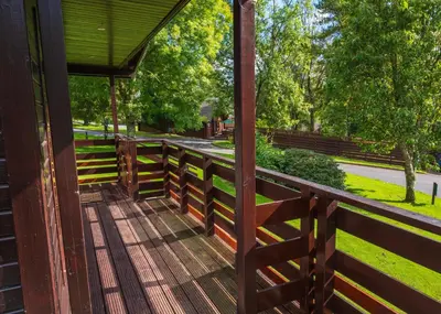 a wooden porch with a fence in a park at Bluebell Lodge 5 with Hot Tub in Newton Stewart