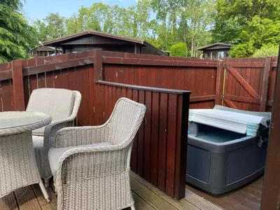 a patio with two chairs and a grill on a deck at Bluebell Lodge 10 with Hot Tub in Newton Stewart