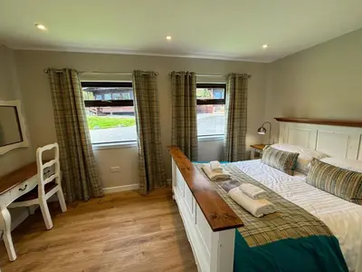 a bedroom with a bed and a desk and two windows at Bluebell Lodge 11 with Hot Tub in Newton Stewart