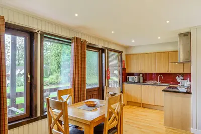 a kitchen with a wooden table and chairs and a window at Birch Lodge 19 with Hot Tub in Newton Stewart