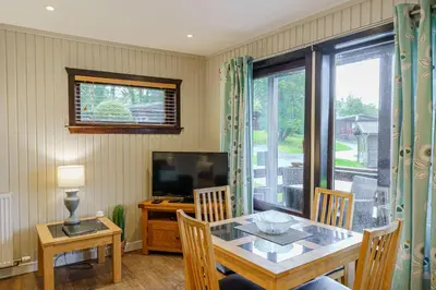 a dining room with a table and a television at Birch Lodge 16 in Newton Stewart