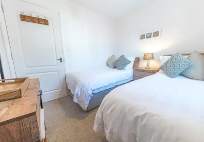 a bedroom with two beds and a dresser with a desk at Lilac Cottage in Keswick