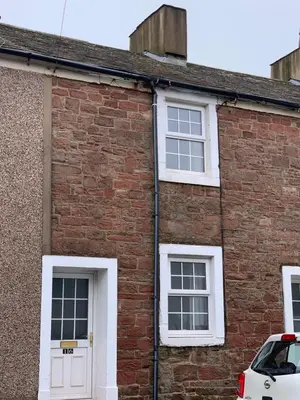 a brick house with white windows and a white car parked in front at 16 Main Street in St Bees