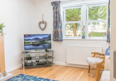 a living room with a flat screen tv and two windows at Riverside View in Keswick
