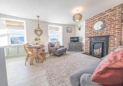 a living room with a fireplace and a table and chairs at Victoria Apartment, Derwent House in Keswick