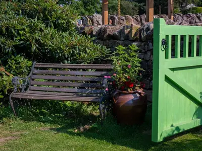 a green bench next to a stone wall with a plant at How Hill Farm Cottage in Penrith