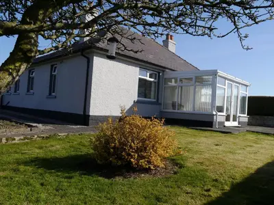 a blue and white house with a tree at Woodhall Cottage in Annan