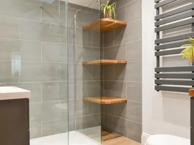 a bathroom with a shower with wooden shelves at Bumble Cottage in Cockermouth