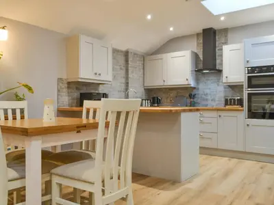 a kitchen with white cabinets and a wooden table and chairs at Bumble Cottage in Cockermouth
