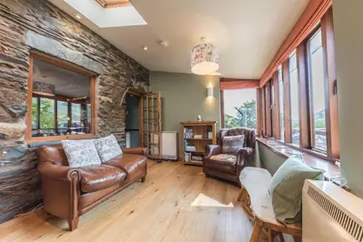 a living room with leather furniture and a stone wall at Slater Bob's Coppermines Valley in Coniston
