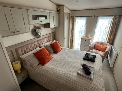 a bedroom with a bed with orange pillows and a chair at Luxury Lake District Holiday Lodge-Sleeps 4 in Cockermouth