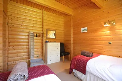 a bedroom with wooden walls with two beds and a desk at Birchlea in Kippford