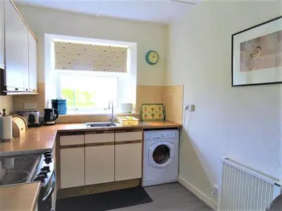 a kitchen with a washing machine and a window at Barnacle in Mainsriddle