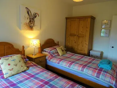 a bedroom with two beds and a lamp and a cabinet at Shelduck Cottage in Mainsriddle