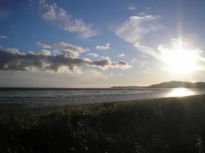 a beach with the sun shining on the water at Shelduck Cottage in Mainsriddle