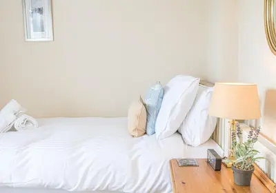 a white bed with white pillows and a table with a lamp at 7 Greta Grove House in Keswick