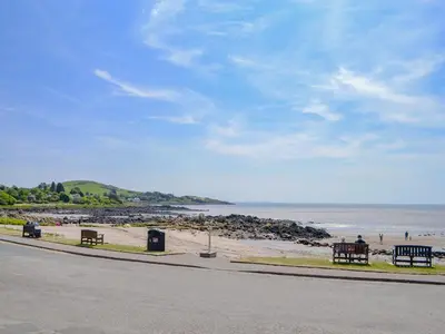 a beach with benches and the ocean on a sunny day at Mossdale in Rockcliffe