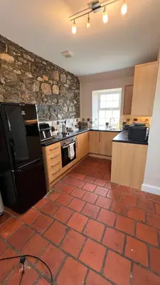 a kitchen with a black refrigerator and a stone wall at Popsal in Kirkcowan