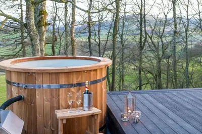 a wooden hot tub on a wooden table with wine glasses at Snowdrop, Penruddock an Eco and dog friendly lodge with hot tub, 10 minutes to Lake Ullswater in Penruddock