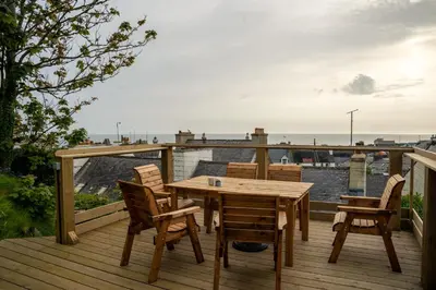 a wooden table and chairs on a deck with a view at The Portpatrick Pad - A cosy 3 bed cottage, w. sea views & garden office in Portpatrick