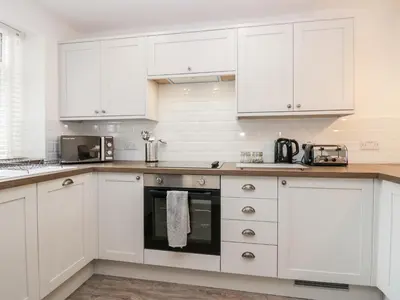 a white kitchen with white cabinets and appliances at Wainwright Cottage in Seascale