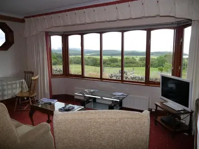 a living room with a large window and a television at Collin Hill House in Castle Douglas