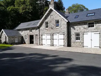 an old stone building with two white garage doors at Rusko Stables in Gatehouse of Fleet