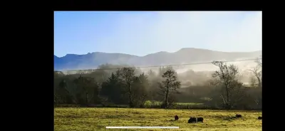 two animals grazing in a field with mountains in the background at Spacious Holiday Home in Cumbria in Arlecdon