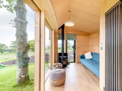 a wooden house with a blue couch and a tree at The Curve At Caerlaverock Estate in Glencaple