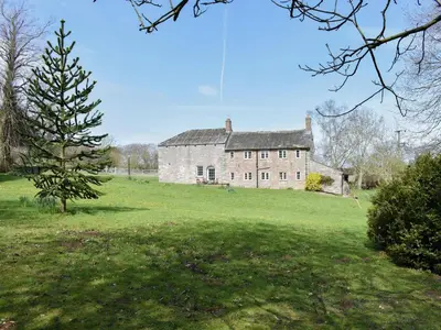 an old stone house in a field with a tree at Rushgill House in Sebergham